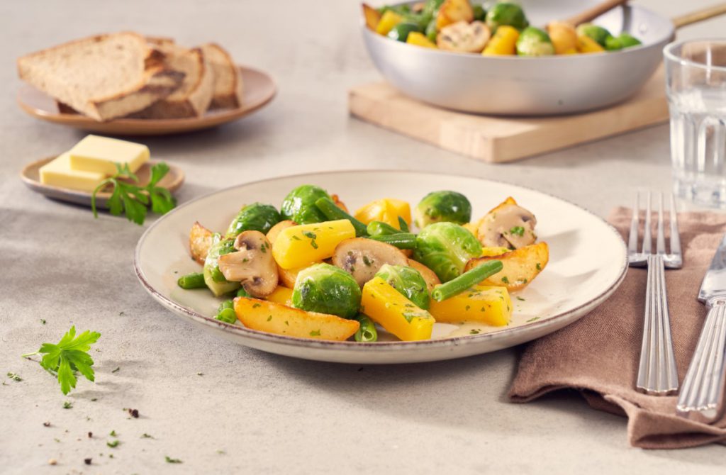 Ein Teller mit gerösteten Kartoffelecken, Rosenkohl, gelber Paprika, grünen Bohnen & Pilzen von FRoSTA Tiefkühlprodukten bringt kartoffeligen Genuss.