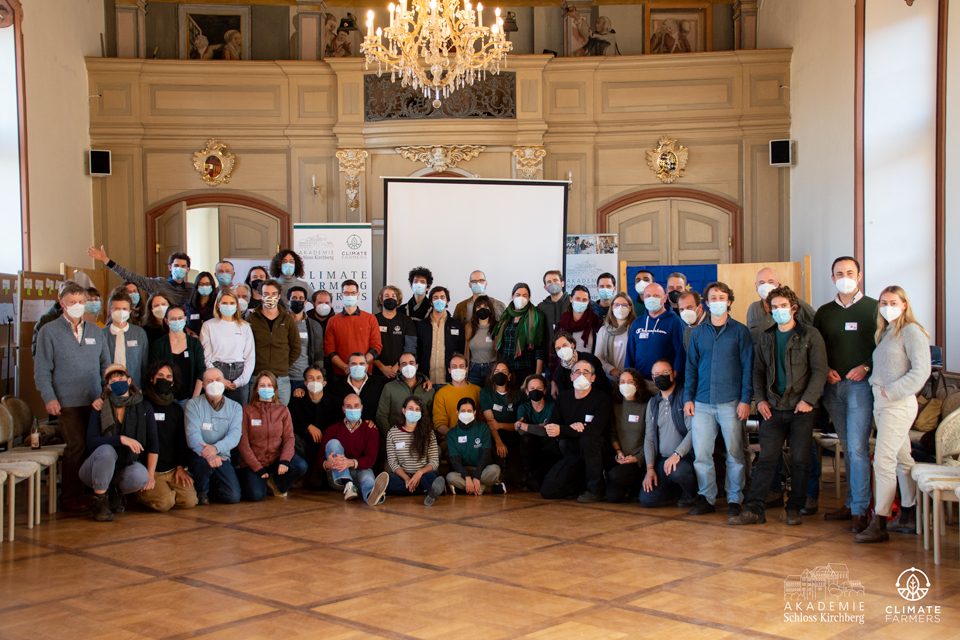 Eine Gruppe mit Masken trägt im eleganten Raum vor Klimabannern zu Carbon Farming; das FRoSTA Logo erscheint neben einer Präsentation zu FRoSTA Tiefkühlprodukten.