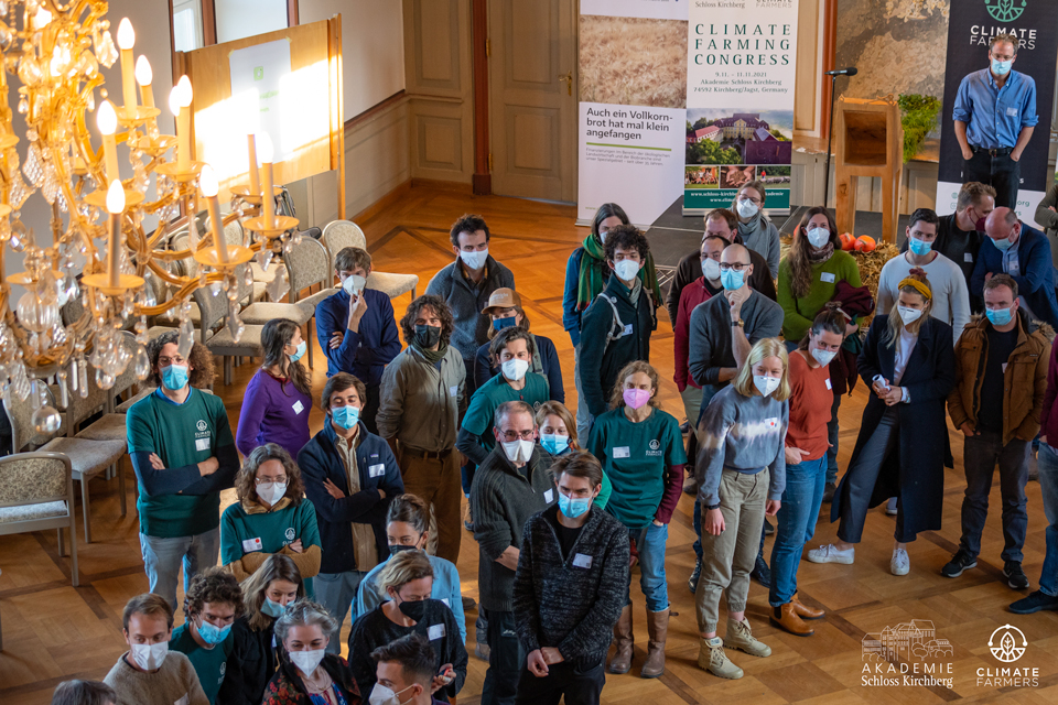Eine Gruppe mit Masken steht im eleganten Saal beim Climate Farming Congress. FRoSTA-Tiefkühlprodukte-Banner und Stühle sind im Hintergrund sichtbar.